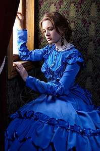 19世纪末穿蓝色旧礼服的年轻女子坐在车窗旁的图片