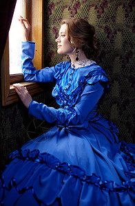 19世纪晚期穿蓝色旧礼服的年轻女子在逆向火车轮图片