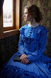 19世纪晚期穿蓝色旧礼服的年轻女子坐在古老铁路列车的曲折里看图片