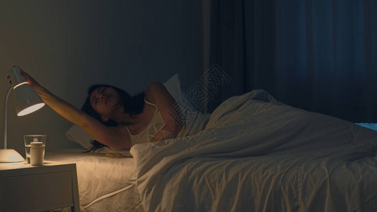 躁动不安印度女手在深夜在家里的房间里关闭床边的电灯开关背景