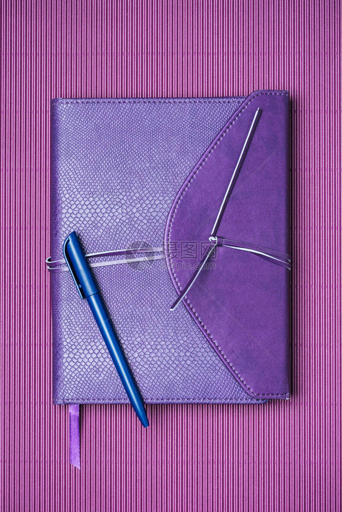 紫色背景上蓝色笔和记本的顶部视图图片