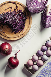紫色卷心菜洋葱和彩蛋在灰色蛋盒中的顶部视图图片