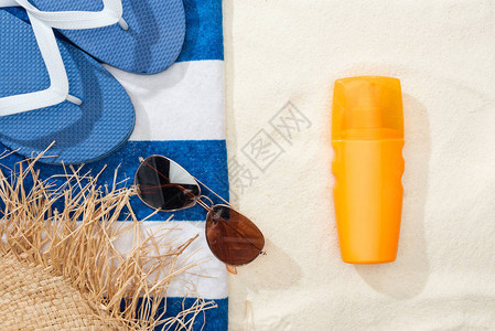 金色沙滩上的防晒霜草帽人字拖太阳镜和蓝白条纹图片