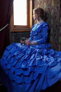穿着蓝旧礼服的年轻女子19世纪末期坐在古老铁路火车的厢里看图片