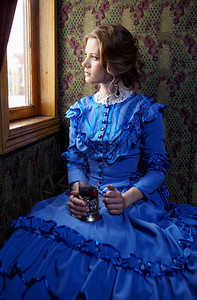 穿着蓝旧礼服的年轻女子19世纪末期坐在古老铁路火车的厢里看图片