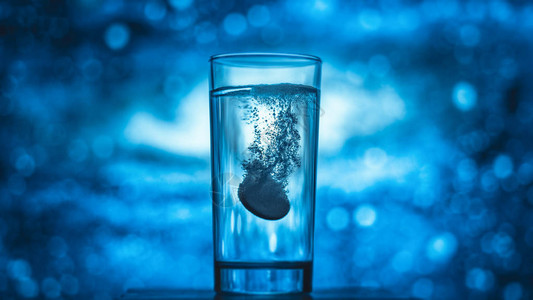 一杯水与蓝色背景上的药丸图片
