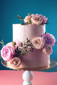 粉红奶油婚礼蛋糕装饰着蓝色背景的鲜玫瑰食图片