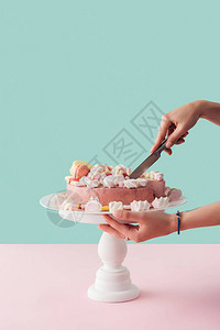 妇女切粉红棉花糖蛋糕时用刀子图片