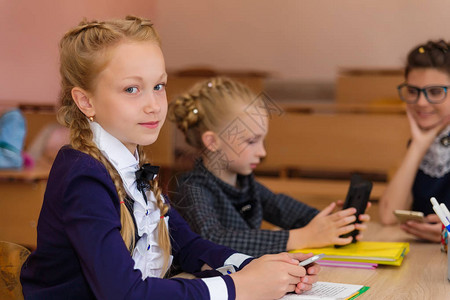 女孩们在课桌旁女朋友们拿着书本笔记本和电话坐在学校里孩子们在图片