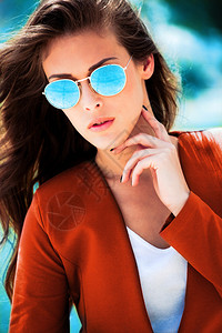 身戴浅蓝色太阳眼镜和橙色外套的城市年轻时装女图片