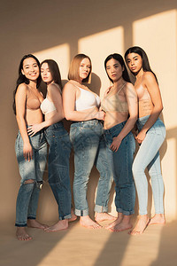 穿着蓝色牛仔裤和胸罩的5名美丽的多文化妇女背景图片
