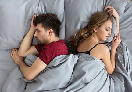 年轻夫妇背靠睡在床上的俯视图图片