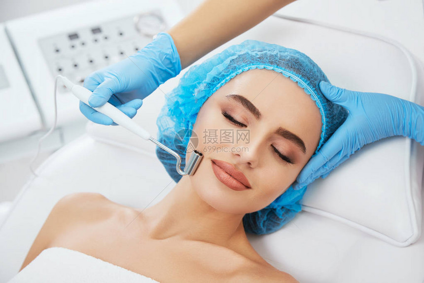 在美容诊所的蓝色帽子躺在沙发上闭着眼睛的女人的头和肩膀图片