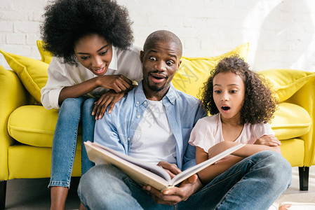 震惊的非洲父母和小女儿一起在家阅读书本图片