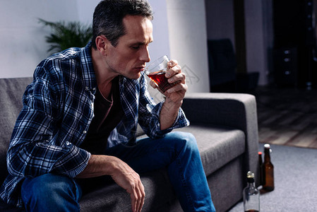 坐在家里沙发上喝着酒的男人的侧视图图片