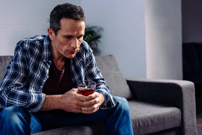 坐在家里沙发上喝着酒的男人的侧视图图片