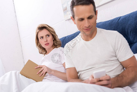 丈夫在床上看书时使用智能手机而妻子图片