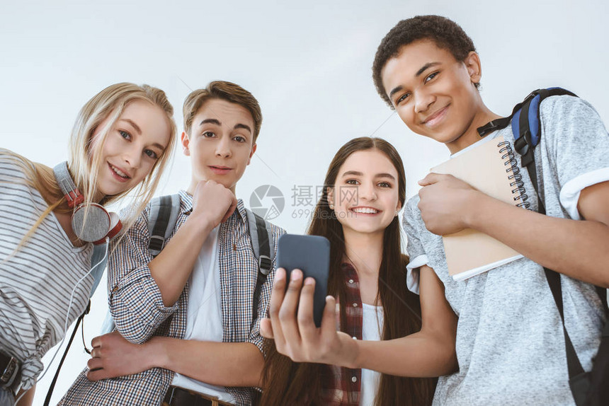 使用智能手机的多文化笑青少年低角度视角图片