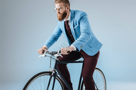 穿着西装的时尚男人坐在蓝色隔离的自行车上图片