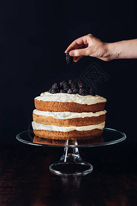 在黑色玻璃柜上装饰美味黑莓蛋糕的女人的图片