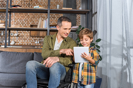 坐在轮椅上快乐的英俊父亲和儿子在家里一起图片