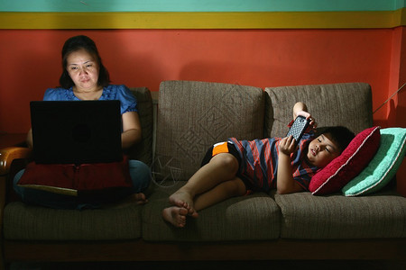 一名妇女使用笔记本电脑的照片和一名青年儿童在沙发上使用平板或智图片