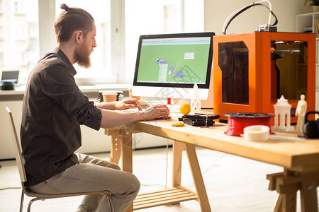 自信的胡须设计师使用计算机程序在3D打印机的帮助下创建原型的剖面图图片
