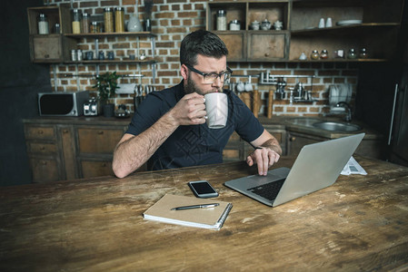 喝咖啡和在家庭办公室用笔记本电脑工作图片