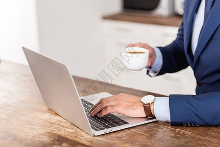 商人拿着咖啡杯和在家使用笔记本电脑拍图片