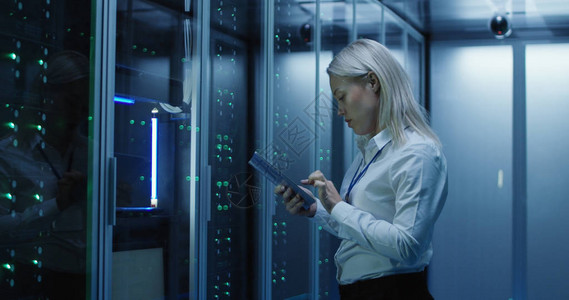 在一个充满机架服务器的数据中心使用平板电脑工作的女技术人员的中照图片