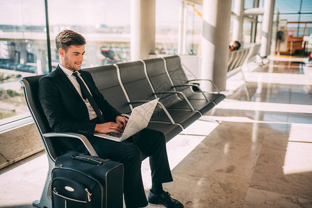 年轻商人坐在上提着手提箱在机场等待航班图片