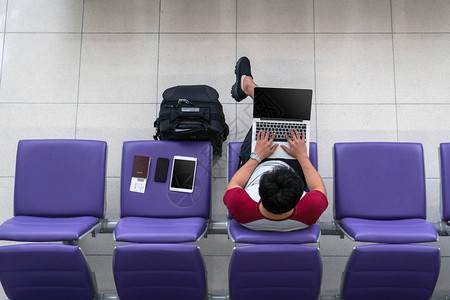 亚洲男旅客在座位上使用带手提箱平板电脑智能手机和护照图片