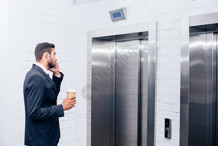 商人通过电话交谈在电梯旁边用一次咖图片