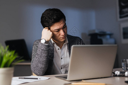 半夜深在黑暗办公室独自加班使用笔记本电脑和手头休息的亚洲困苦男人的肖图片