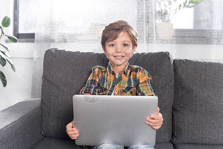 可爱的小男孩膝上型电脑坐在沙发上图片