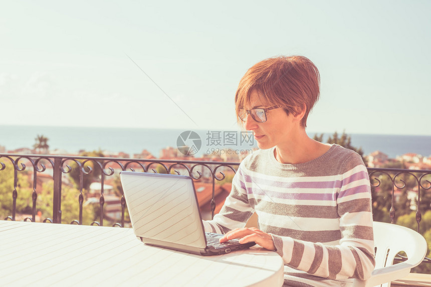 戴眼镜和休闲服装在户外露台上的笔记本电脑上工作的女人在家工作的概念自然采光图片