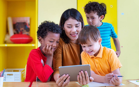 亚洲老师和她的学生在一所国际幼儿园一起看平板电脑图片