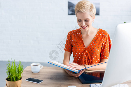 家庭办公室带图形平板和计算机的桌边女自由职业者阅读书手持图图片