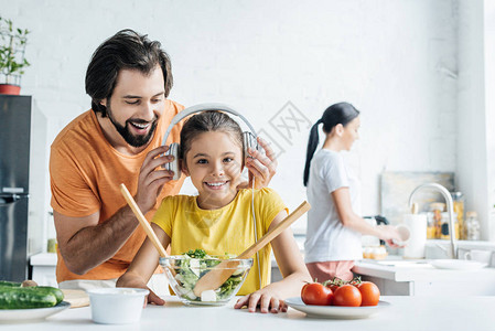 微笑的父亲和快乐的女儿戴着耳机一起做饭图片