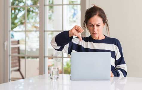 中年妇女在家里使用笔记本电脑时脸色愤怒图片