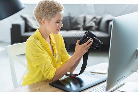 女摄影师用图形平板电脑和照相机在桌子上观看摄像屏幕的妇女背景图片