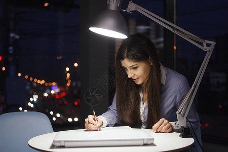 晚上在办公室用台灯在桌子上工作的女商人图片