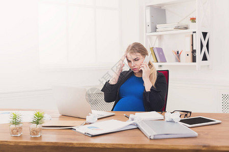 怀孕的商务女士在工作中谈电话忧心忡的女商人坐在办公室的工作地图片