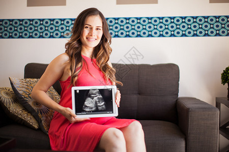 快乐的年轻女子期待一个孩子并展示她的婴儿超声波图片