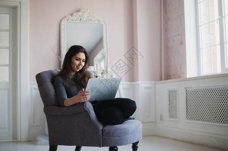 在家的年轻女士坐在椅子上用笔记本电脑图片