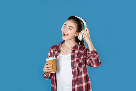 年轻女孩用耳机听音乐并喝着咖啡在图片