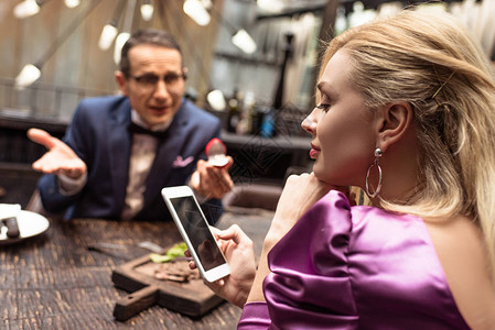 男人在餐厅用智能手机时求婚女友的男伴图片