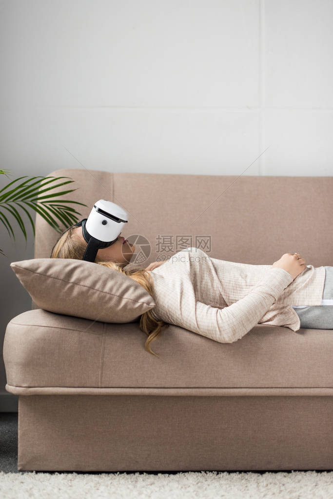 坐在沙发上的虚拟现实头盔中的年轻女图片