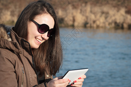 年轻女子女孩在户外坐在河边的长凳上微笑着使用平板电脑图片