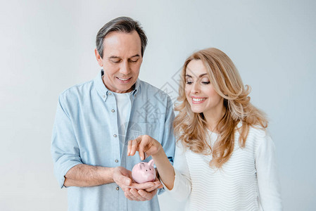 微笑的中年夫妇把硬币投进小猪银行在图片